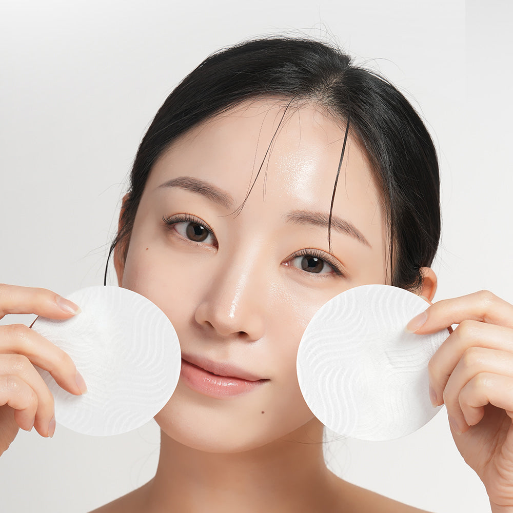 Woman holding BARULAB Rice Bran Ceramide Cream In Cleansing Pads 30 sheets near her face, showcasing skincare product application.