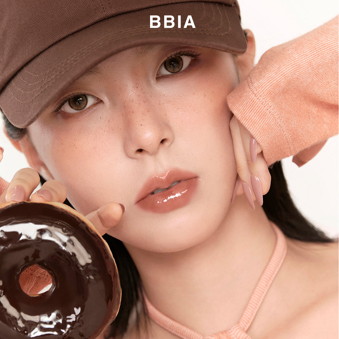 Model wearing BBIA Over Glaze Stick with a glossy finish holding a chocolate donut.
