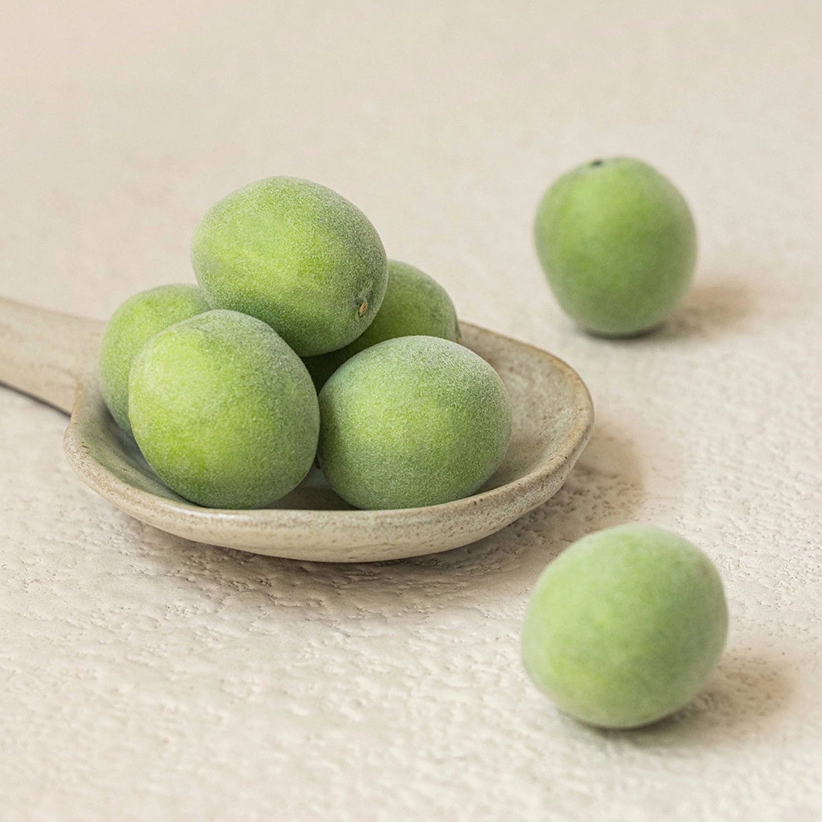 Fresh green plums on a wooden spoon, featured in BEAUTY OF JOSEON Green Plum Refreshing Toner AHA + BHA 150ml.