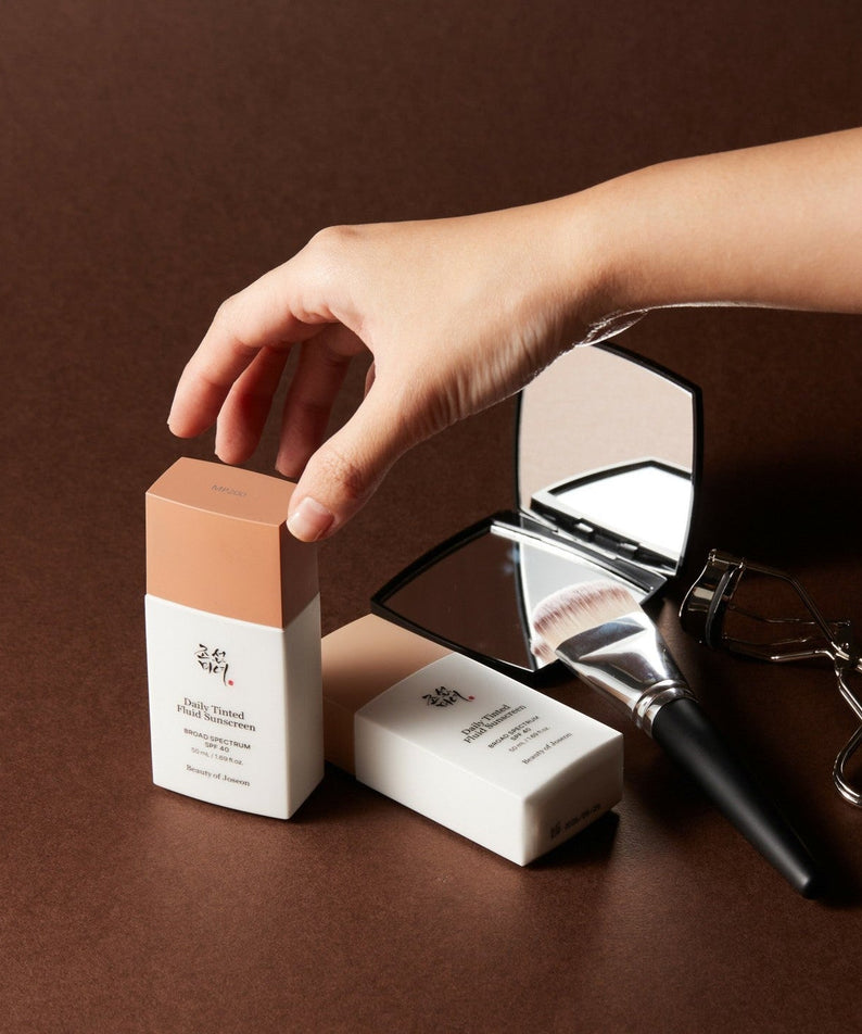 BEAUTY OF JOSEON Daily Tinted Fluid Sunscreen 50ml with mirror and makeup tools on brown surface