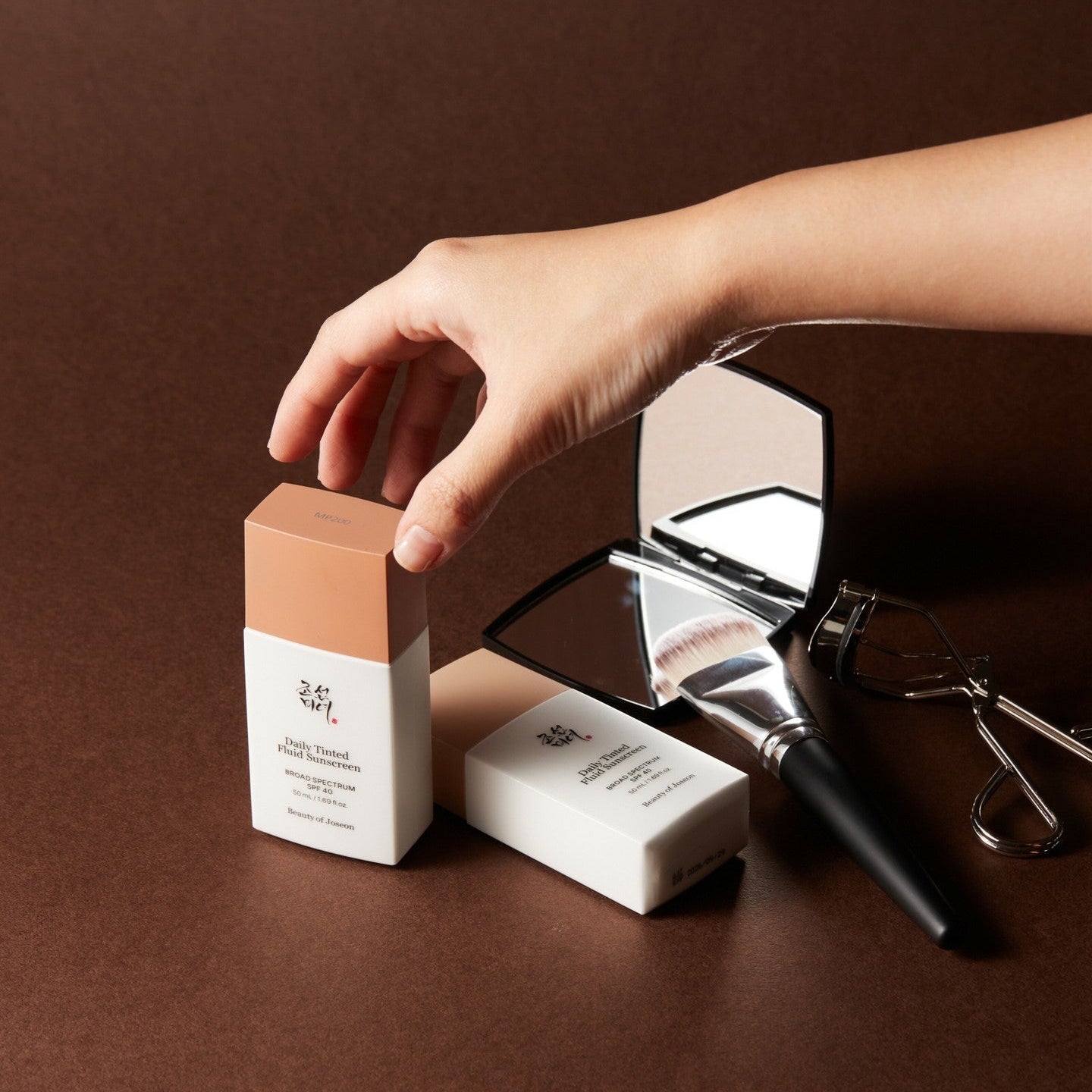 BEAUTY OF JOSEON Daily Tinted Fluid Sunscreen 50ml with mirror and makeup tools on brown surface