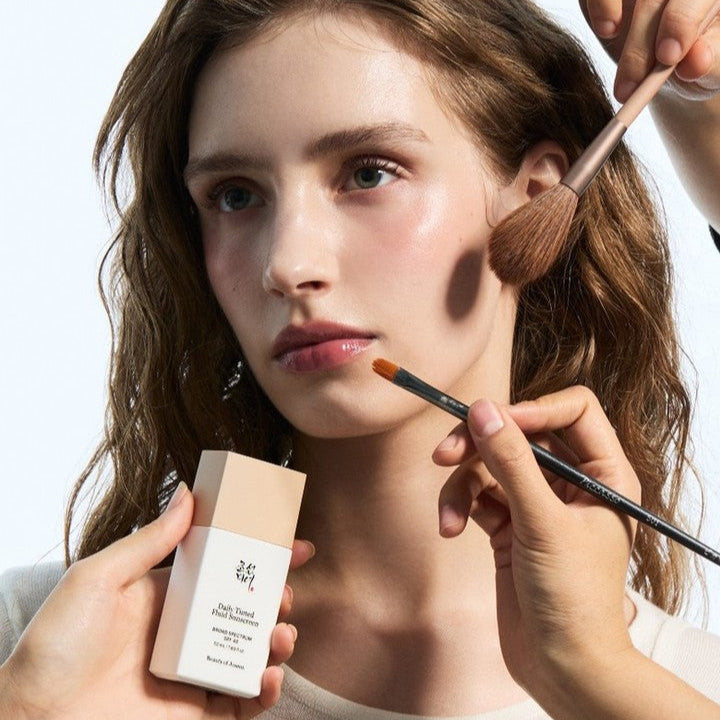 Model applying BEAUTY OF JOSEON Daily Tinted Fluid Sunscreen 50ml with makeup brushes
