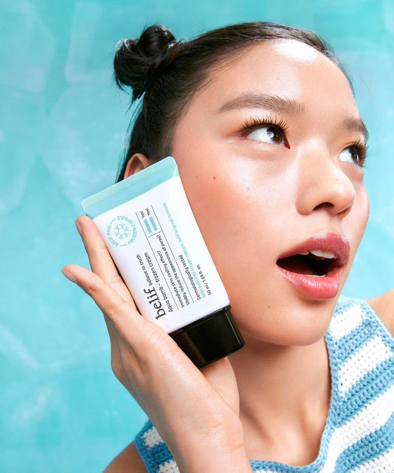 Person holding BELIF Aqua Bomb Frozen Cream 50ml against a blue background.
