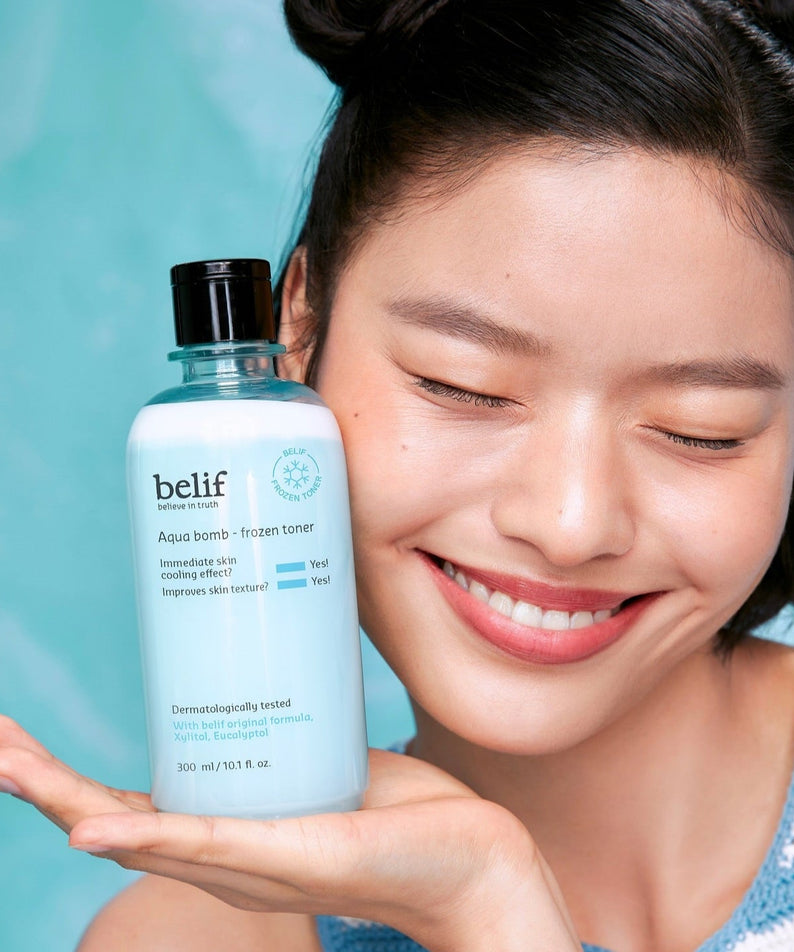Woman holding BELIF Aqua Bomb Frozen Toner 330ml with a blue background.
