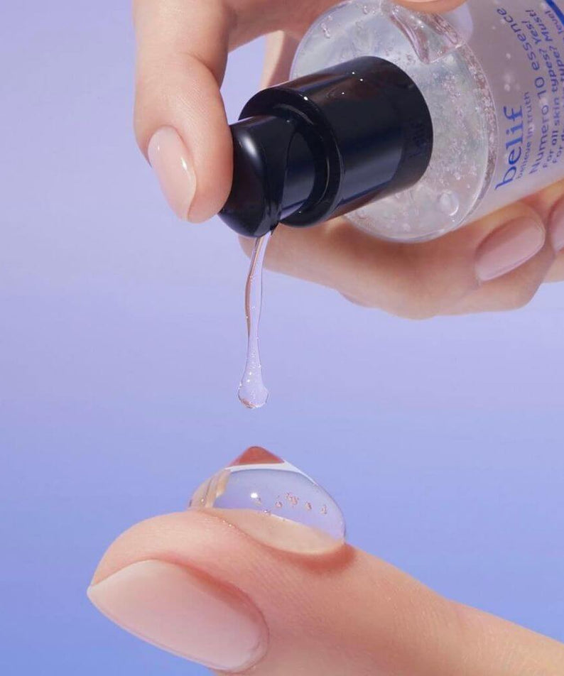 Person dispensing BELIF Numero 10 Essence 125ml onto finger, showcasing texture and consistency of skincare product.