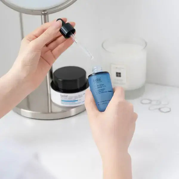 Applying BELIF Super Drops-Hyalucid 11% 30ml with a dropper in hand, skincare routine displayed in a bathroom setting.