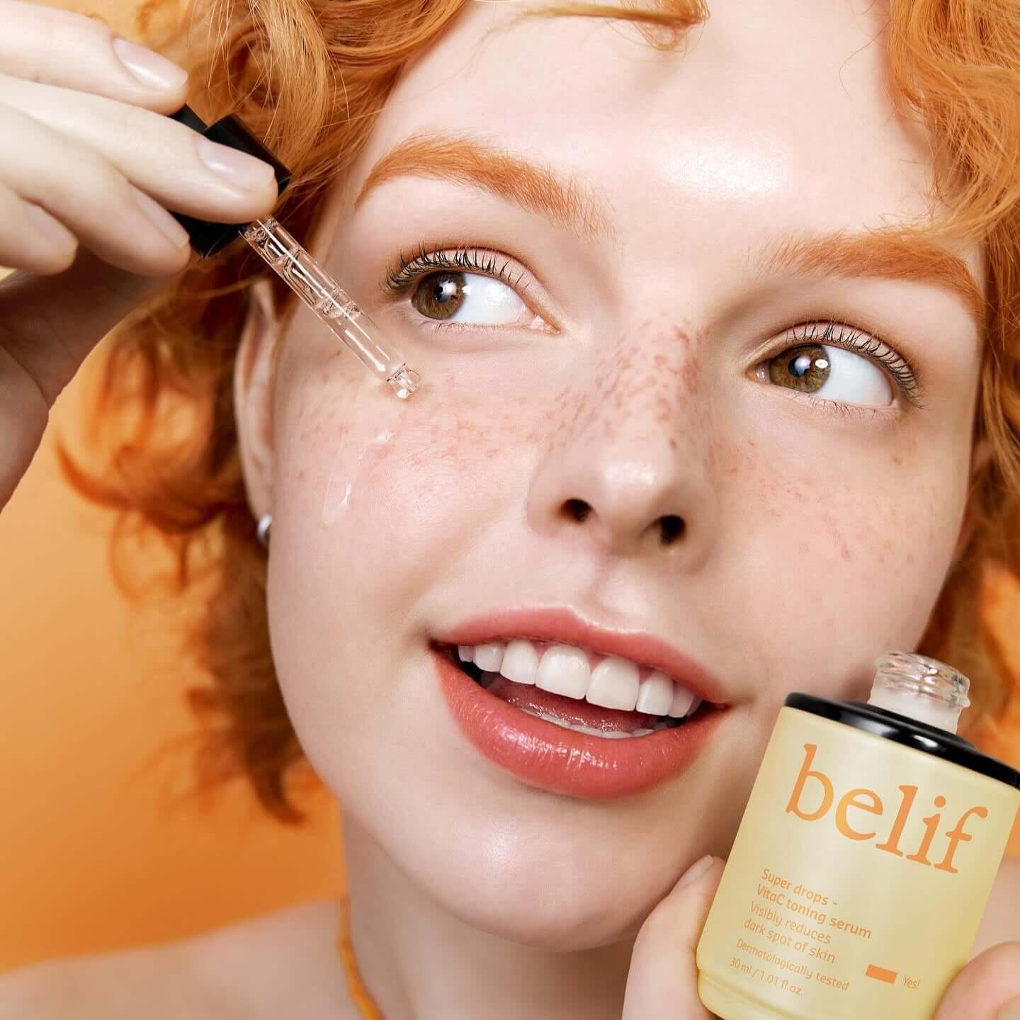 Woman applying BELIF Super Drops Vita C Toning Serum 30ml to her face with dropper from the bottle.
