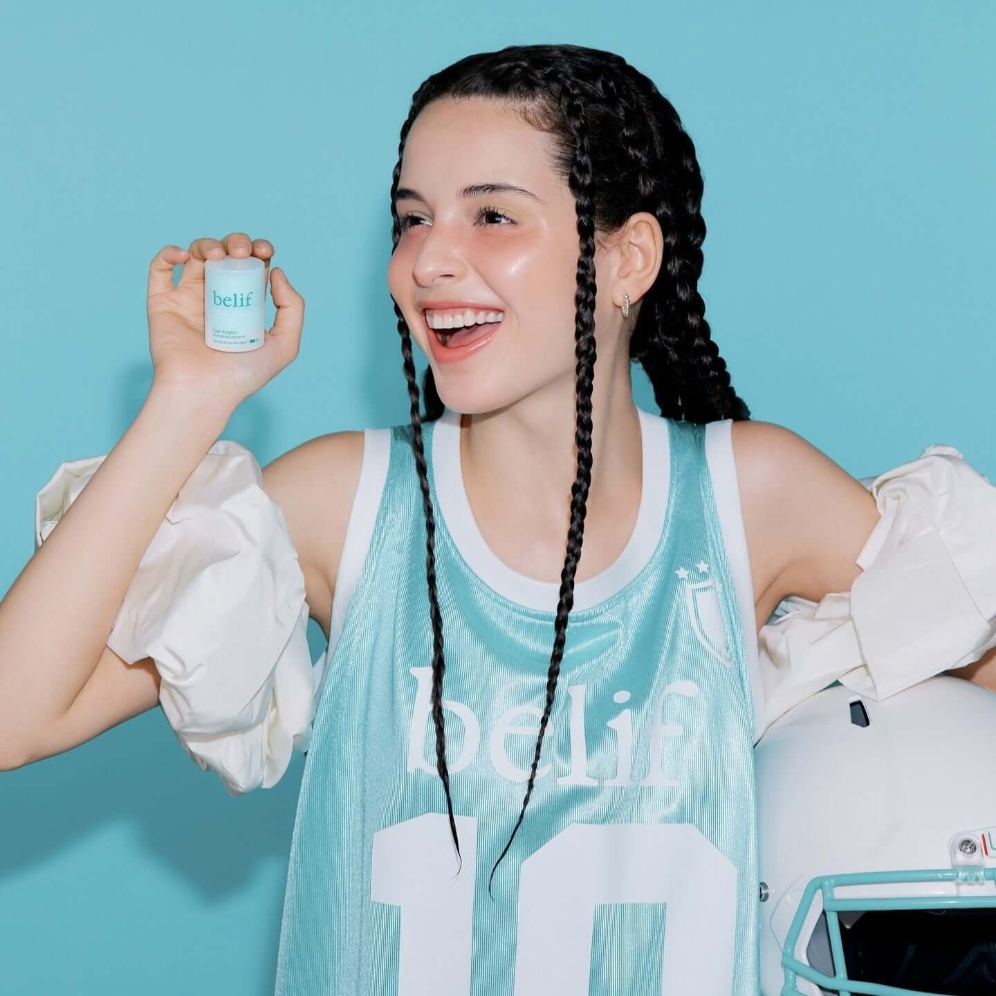 BELIF Super Knight Mint Plumping Lipcerine held by a person in a sports jersey, smiling against a blue background.