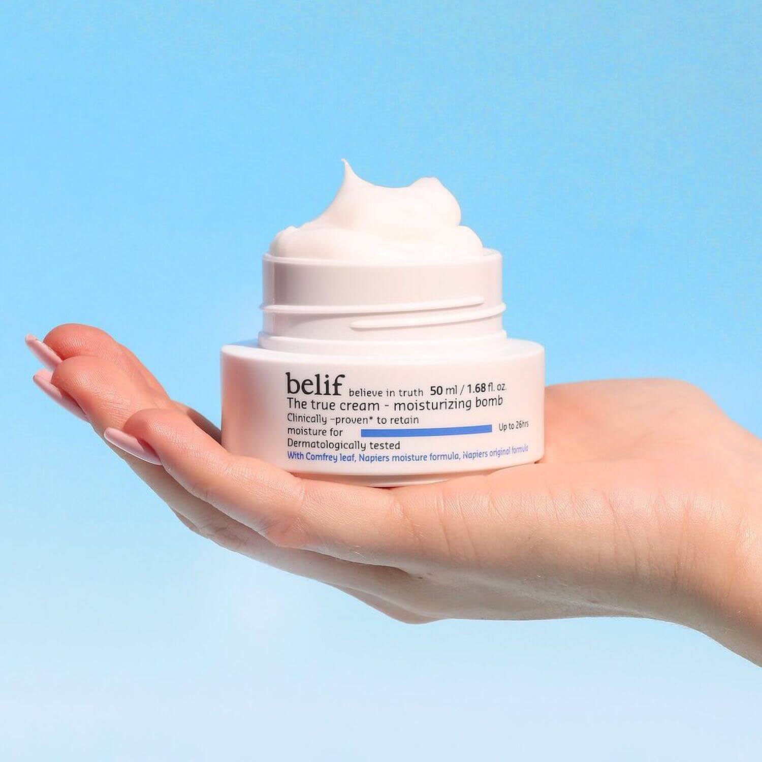 Person holding BELIF The True Cream Moisturizing Bomb 50ml jar with creamy texture, illustrating skincare product's moisturizing benefits.