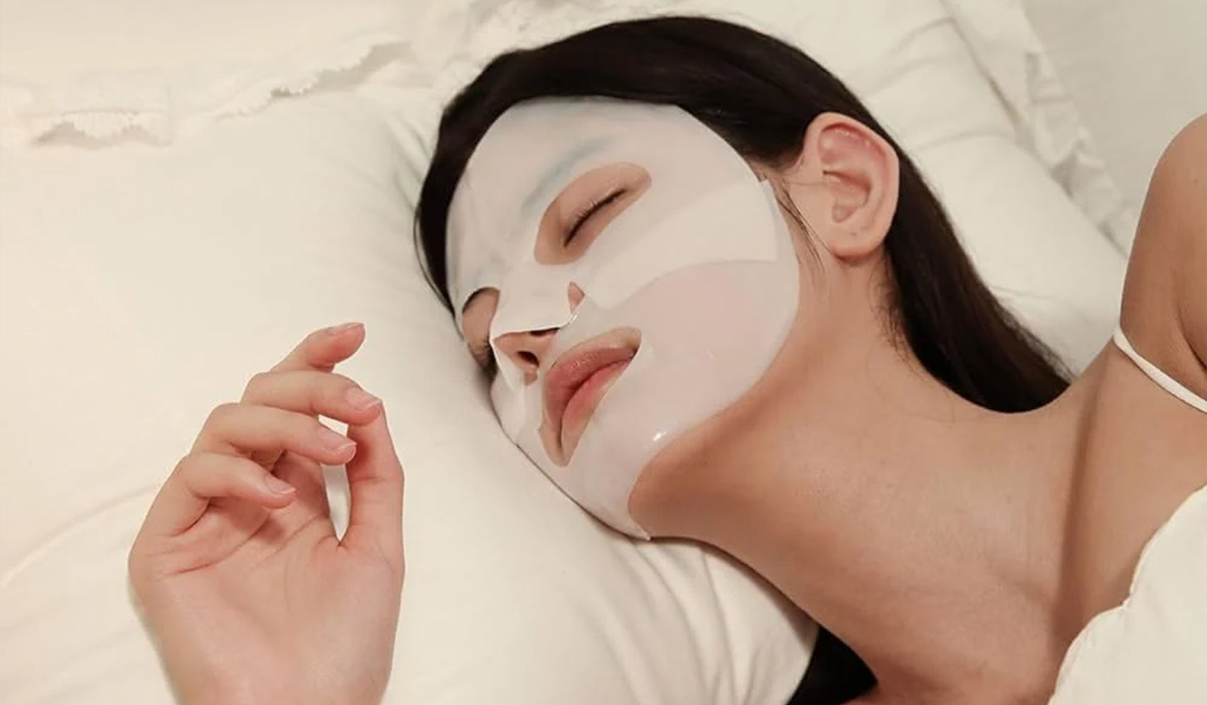 Woman wearing a facial sheet mask while resting on a white pillow for skincare