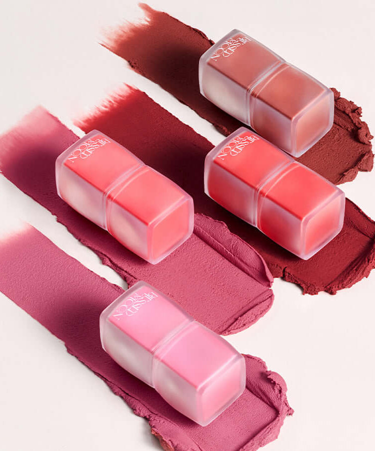 Assorted shades of BLESSED MOON Veil Blur Lip Tint on a textured surface.