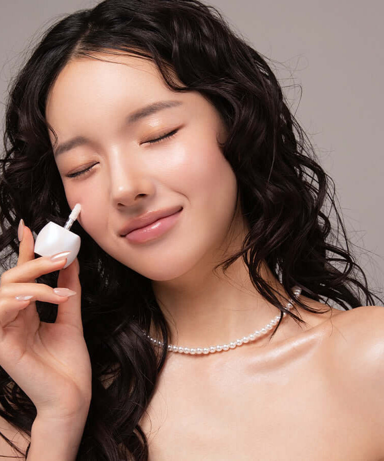 Woman applying BLESSED MOON Veil Melting Glass Highlighter to her cheek, demonstrating a radiant and glowing makeup look