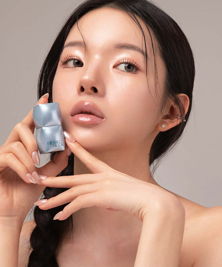 Model showcasing BLESSED MOON Veil Mood Lip Gloss on her lips with product in hand, emphasizing glossy finish and stylish design.