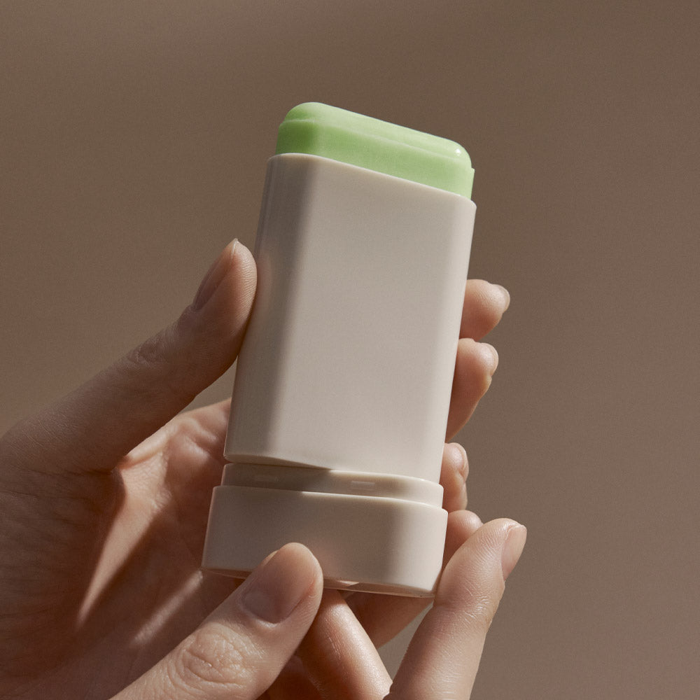 BLITHE Ice Sunscreen Stick held in hand, showing the product's design and green top in a neutral background setting.