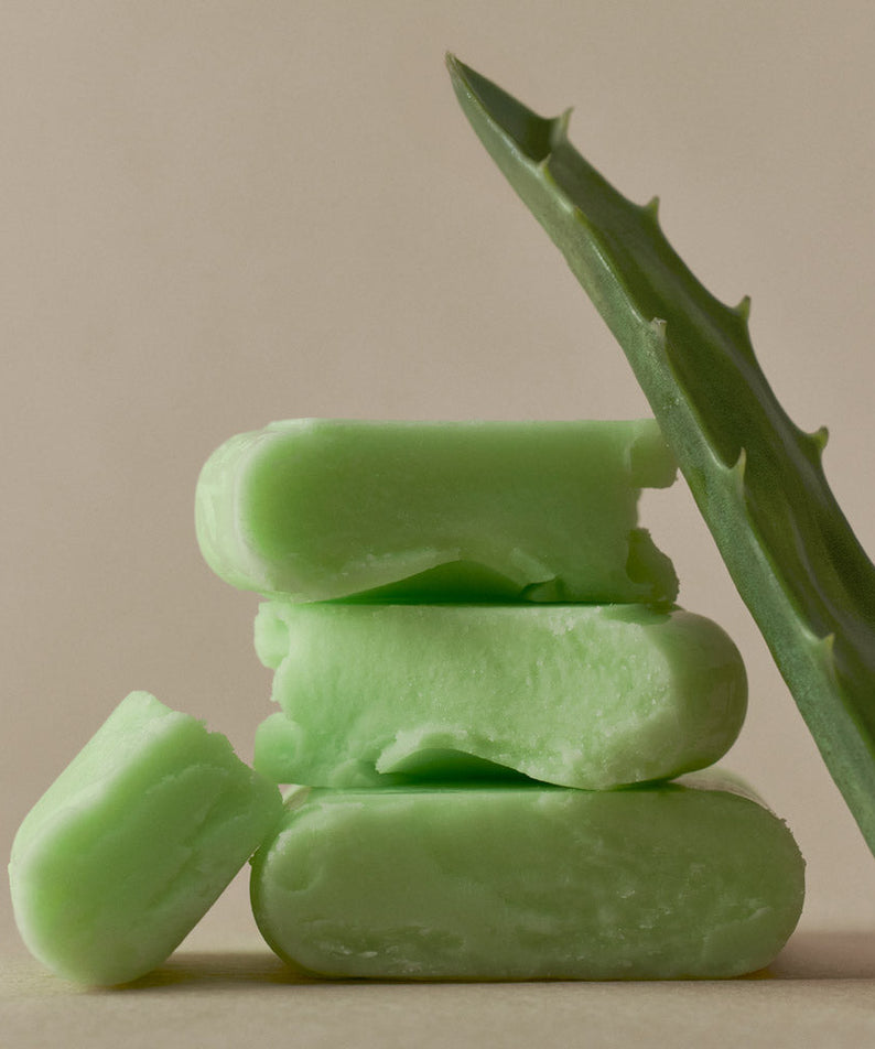 Green aloe vera soap bars stacked with aloe leaf on beige background.