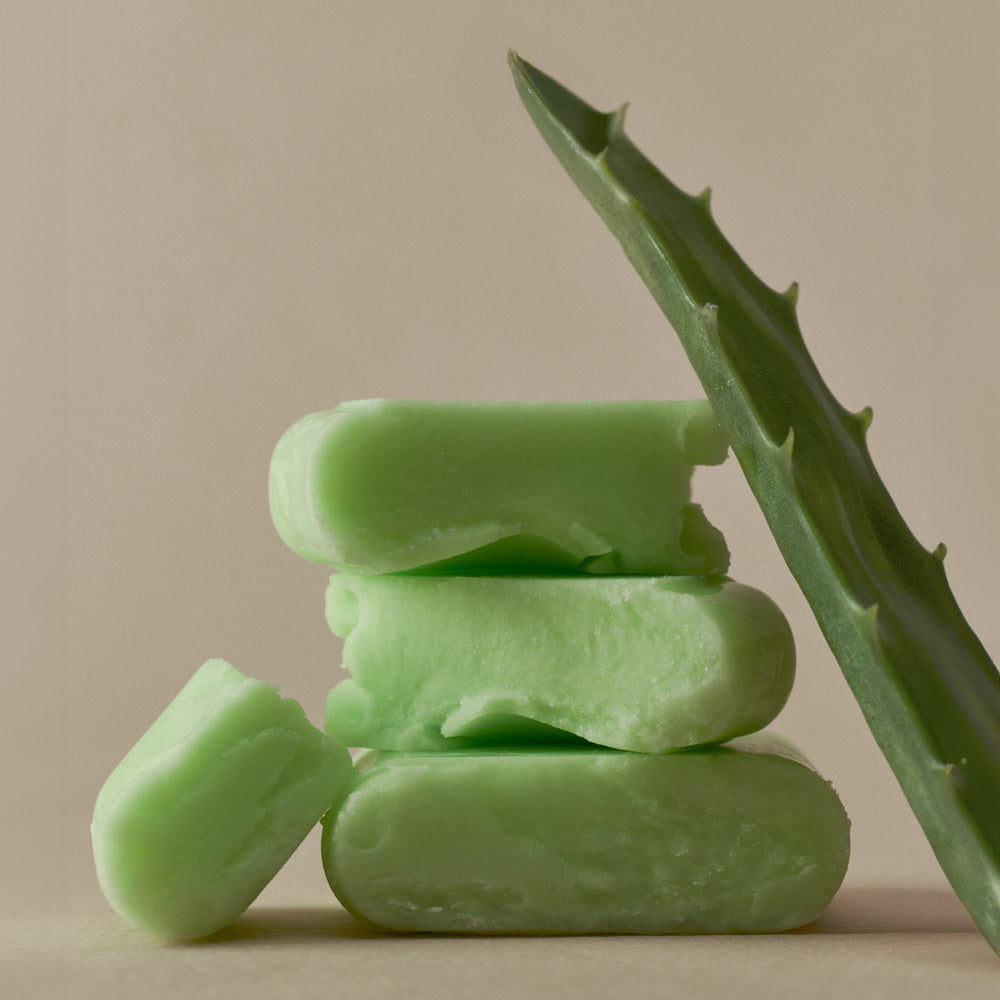 Green aloe vera soap bars stacked with aloe leaf on beige background.