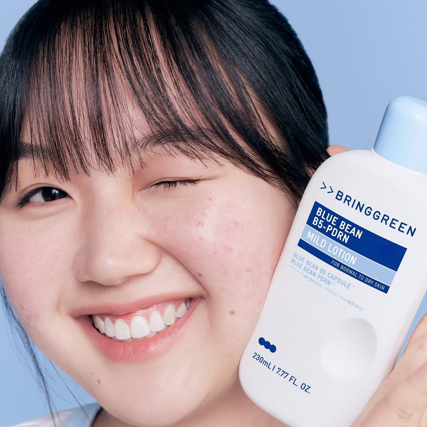 Person holding BRINGGREEN Blue Bean B5-PDRN Mild Lotion 230ml bottle with eyes closed and smiling