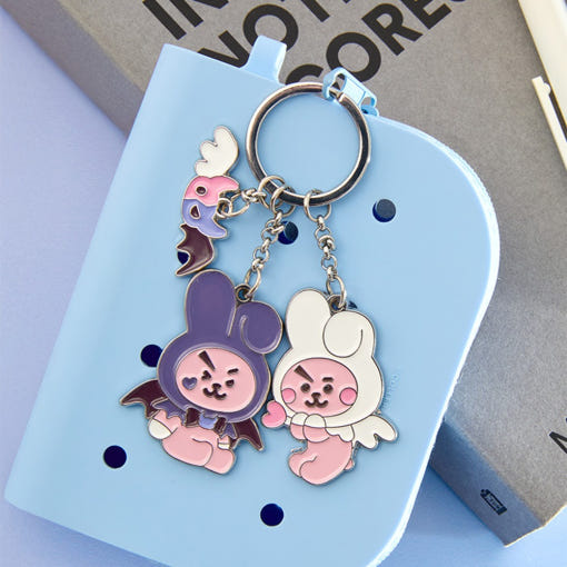 Porte-clés en métal BT21 Angel & Villain sur cahier bleu, design mignon avec personnages ange et méchant, accessoire tendance.