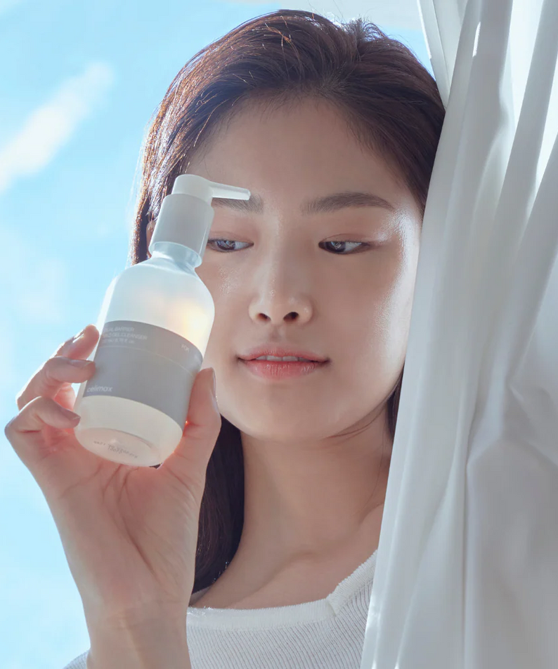 Woman holding CELIMAX Dual Barrier Mild Gel Cleanser 200ml by a window.