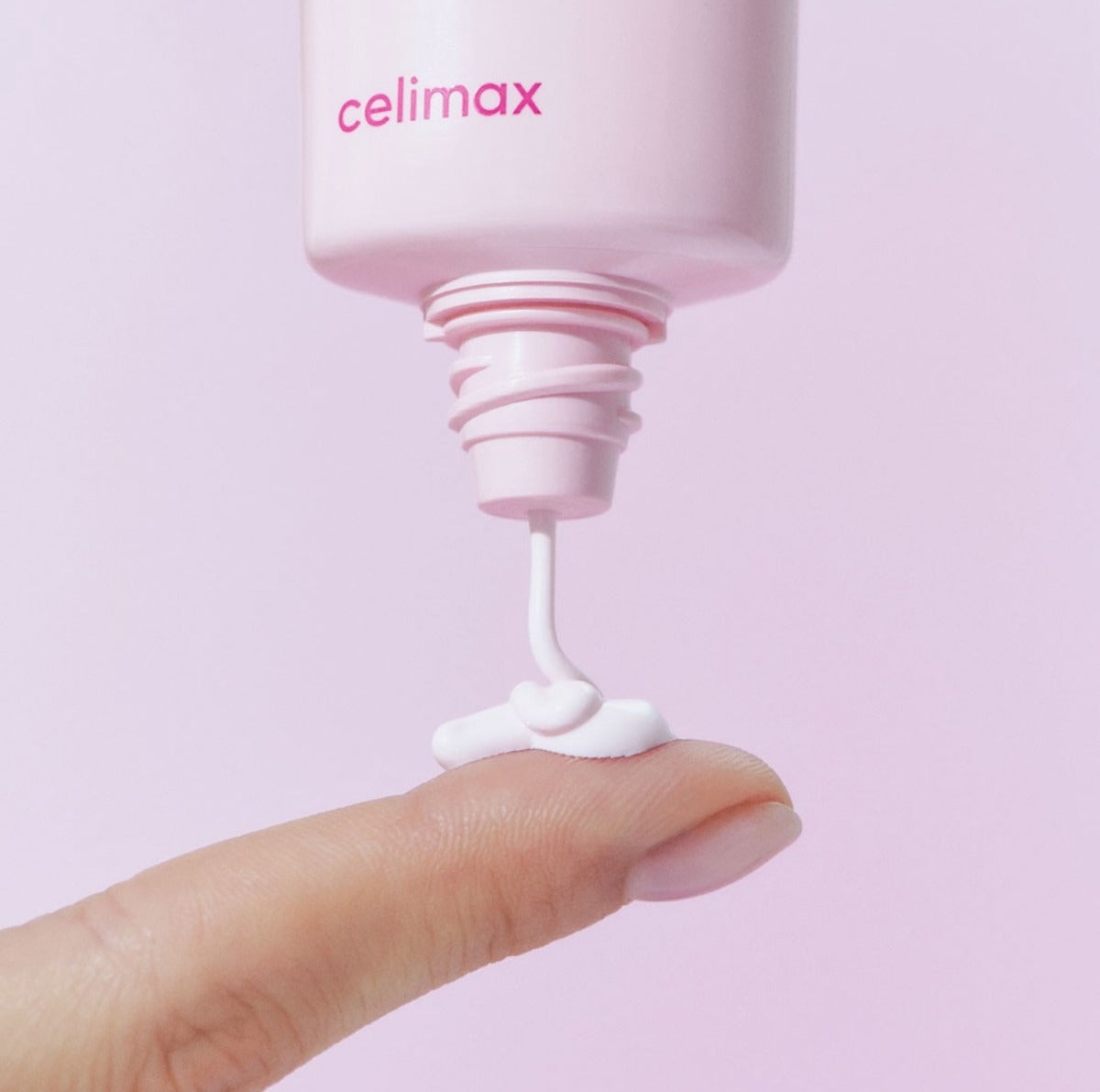 CELIMAX Heart Pink Tone-up Sun Cream 40ml being applied to a fingertip, showcasing its texture and packaging.