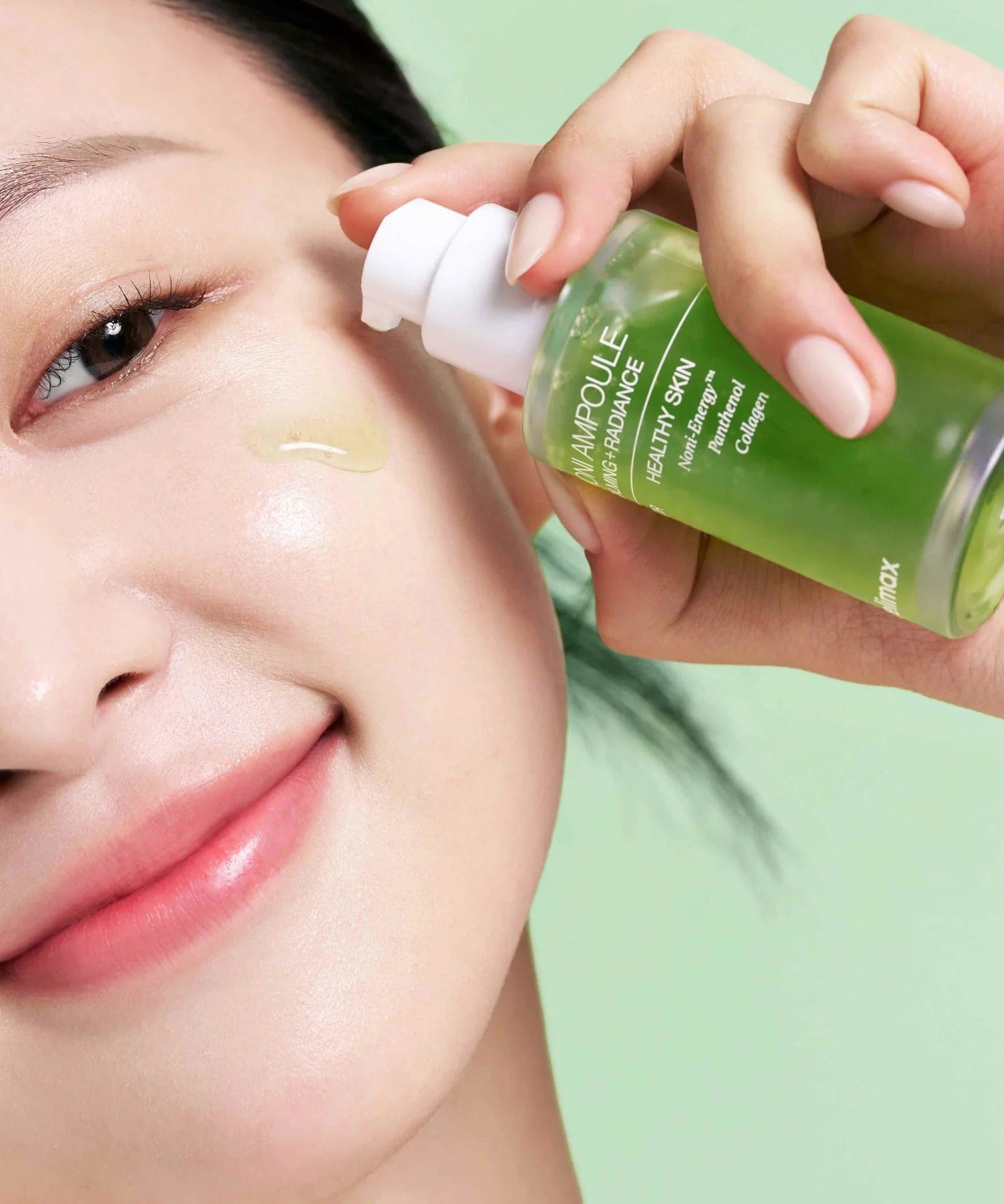 Smiling woman applying CELIMAX Noni Ampoule Calming+Radiance 100ml to her face for glowing skin.