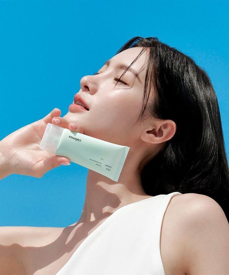 Woman holding CELIMAX The Real Cica Soothing Cream 50ml against a blue sky
