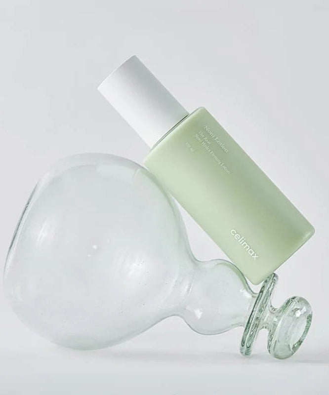 CELIMAX The Real Nino Hydra Firming Lotion 150ml bottle leaning against a glass object on a white background