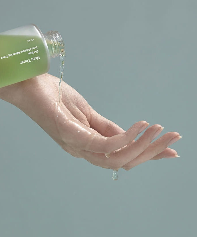 CELIMAX The Real Noni Moisture Balancing Toner 150ml being poured onto a hand, showcasing the texture and consistency of the product.