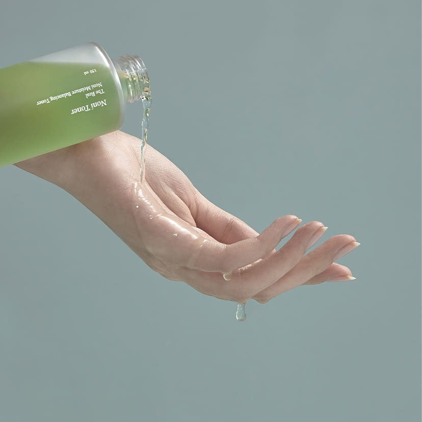 Person pouring CELIMAX The Real Noni Moisture Balancing Toner 320ml onto hand for skincare routine.