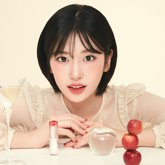 Model with CLIO Crystal Glam Balm, surrounded by clear and red apples, showcasing the elegance and allure of the beauty product.