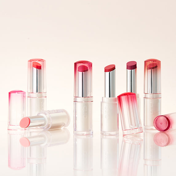 Assorted shades of CLIO Crystal Glam Balm lipstick products arranged on a reflective surface.