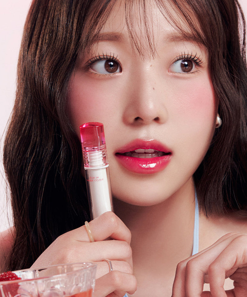 Woman holding CLIO Crystal Glam Tint with glossy lips, showcasing the vibrant effect of the lip product.