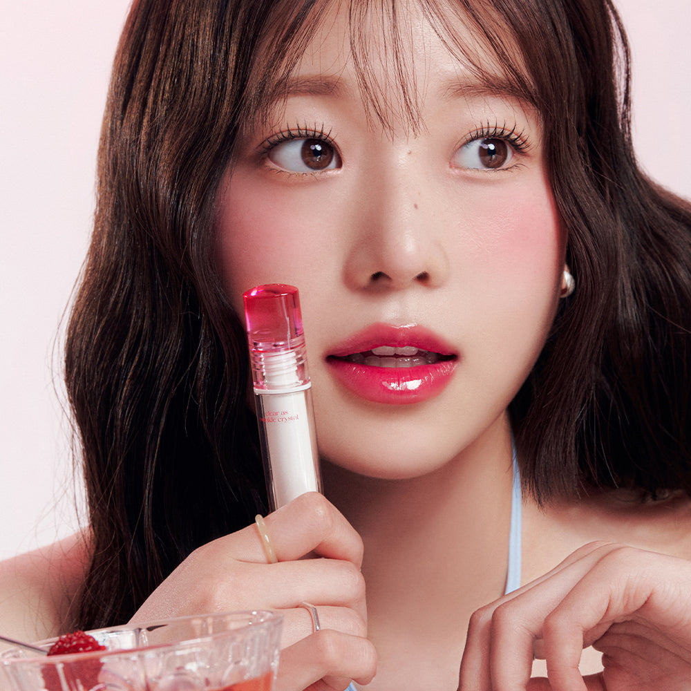 Woman holding CLIO Crystal Glam Tint with glossy lips, showcasing the vibrant effect of the lip product.