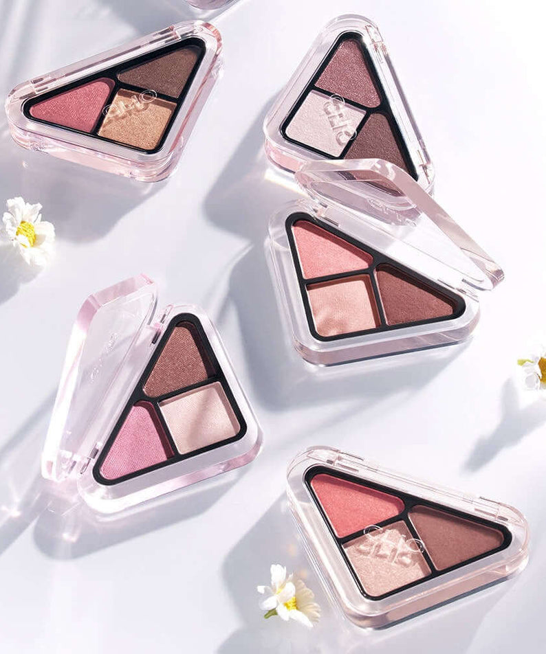 CLIO Essentail Shadow Tab makeup palettes with delicate colors and compact design, surrounded by small flowers on a white background.