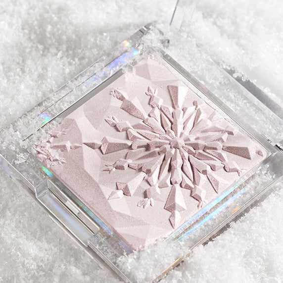 CLIO Prism Highlighter in snow-themed packaging with intricate snowflake design on the powder surface, showcasing its luminous texture.