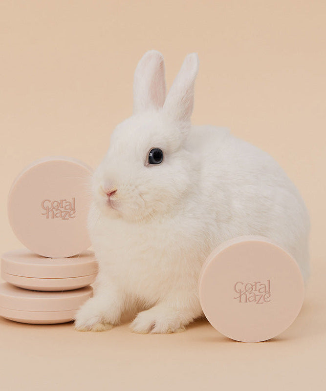 Cute rabbit with CORALHAZE Fixing Blur Cushion SPF50 PA++++ 13g on display, showcasing its soft beige packaging.
