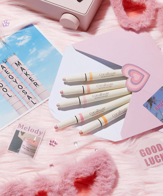 CORALHAZE Idol Aegyo Sal Maker beauty set with pastel packaging on pink fluffy background, enhancing eye makeup for a youthful look.