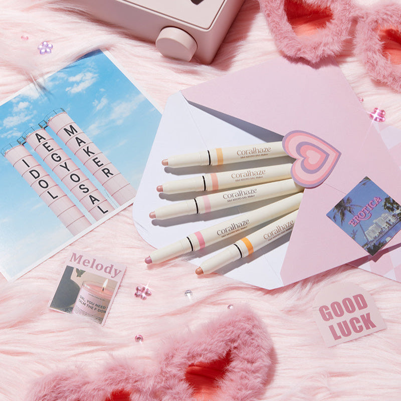 CORALHAZE Idol Aegyo Sal Maker beauty set with pastel packaging on pink fluffy background, enhancing eye makeup for a youthful look.