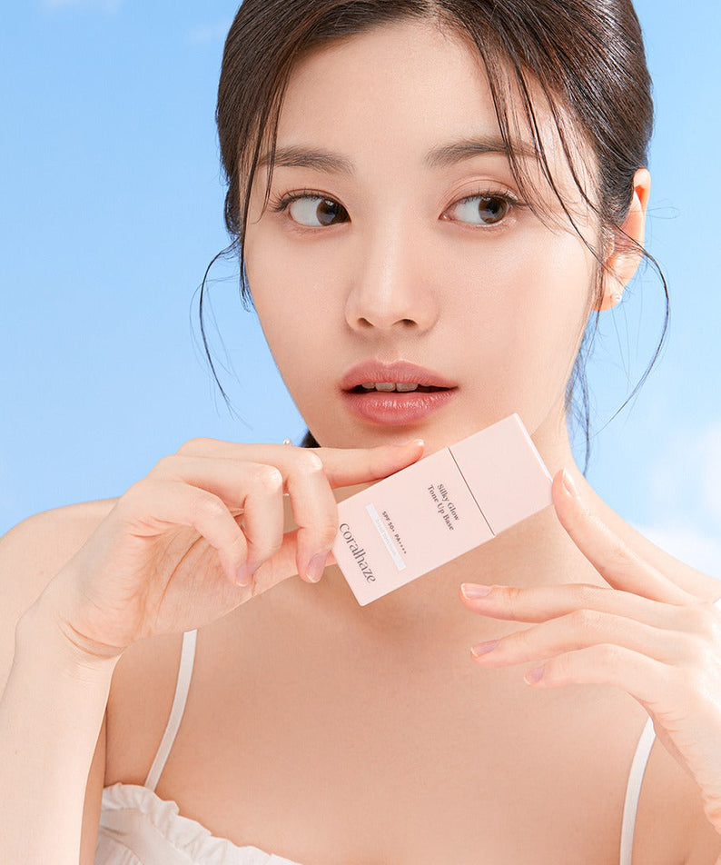 Woman holding CORALHAZE SIlky Glow Tone Up Base against a blue sky background.