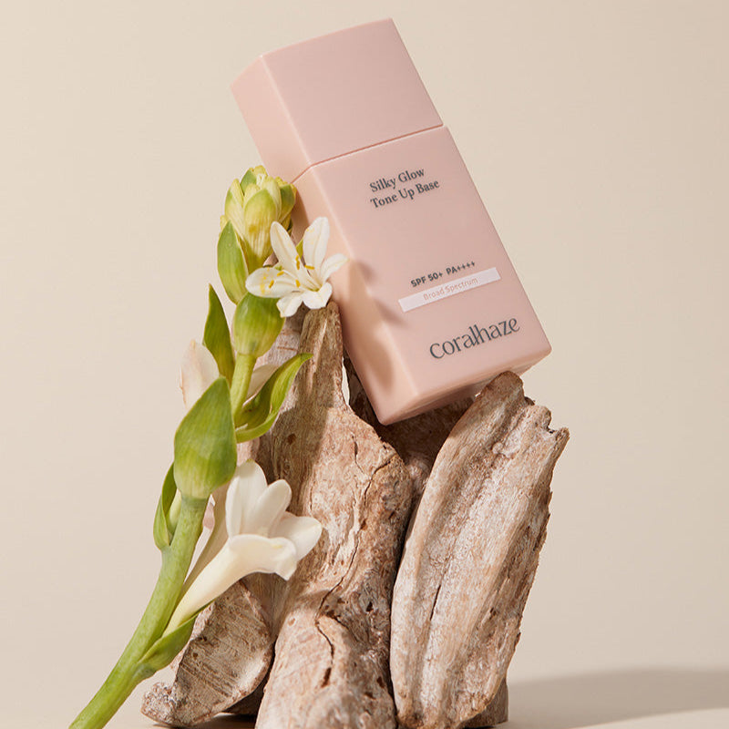 CORALHAZE SIlky Glow Tone Up Base displayed with flowers on wooden pieces.