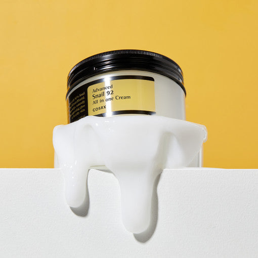 COSRX Advanced Snail 92 All In One Cream 100g jar with cream overflowing on yellow background