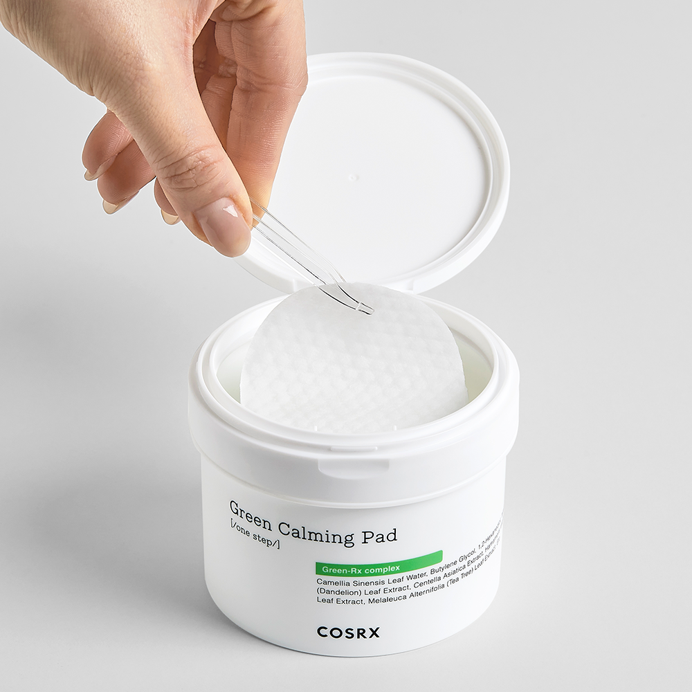 Hand holding a COSRX Green Calming Pad 140ml above the container