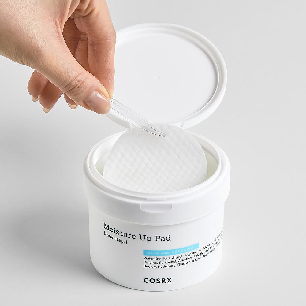 Hand using COSRX Moisture Up Pad 140ml for skincare, showing open container and texture of pads.
