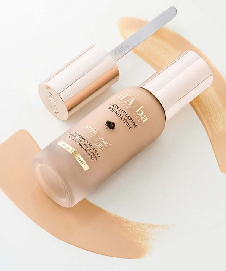 D'ALBA Vegan Skin Fit Serum Foundation bottle with applicator on a background of foundation swatches.