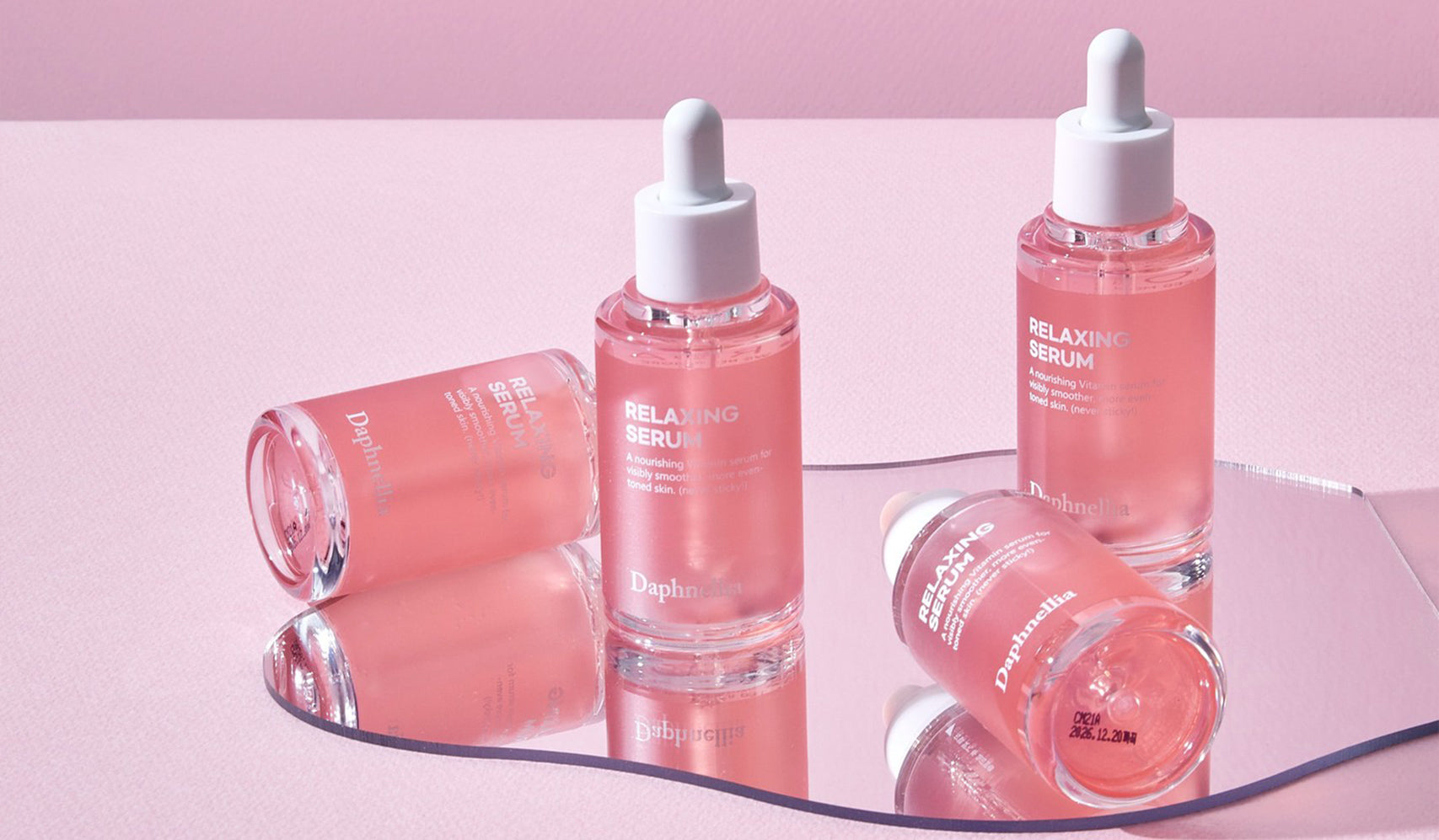 Four pink bottles of relaxing serum on a mirror and pink background