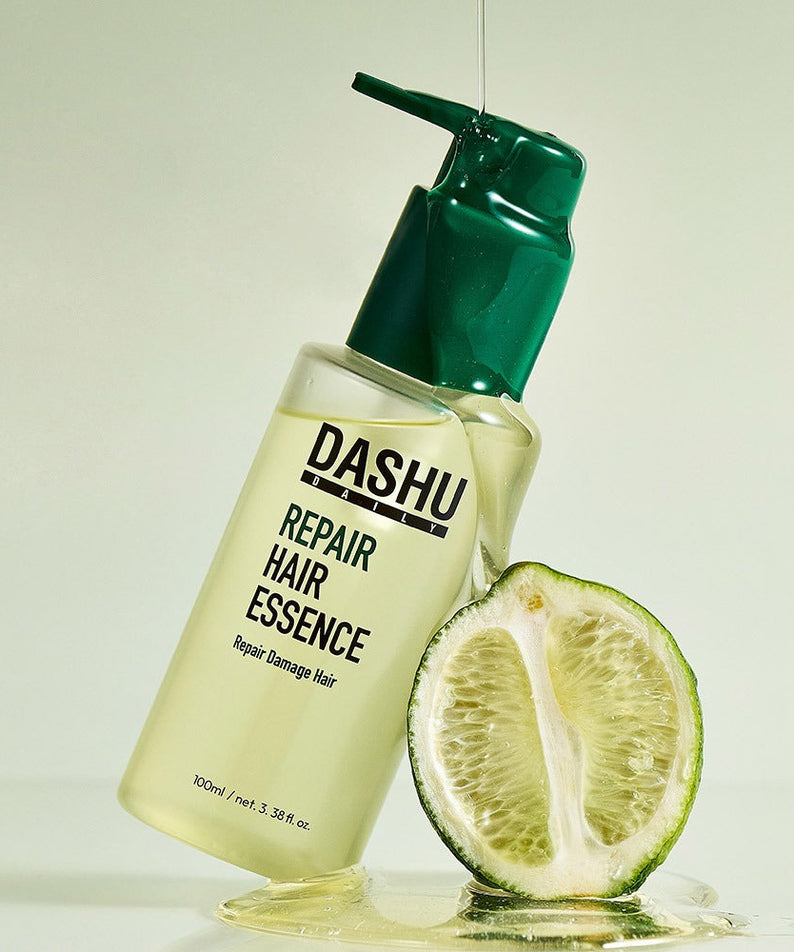 DASHU Daily Repair Hair Essence 100ml bottle with green cap next to a sliced lime, promoting hair repair benefits.