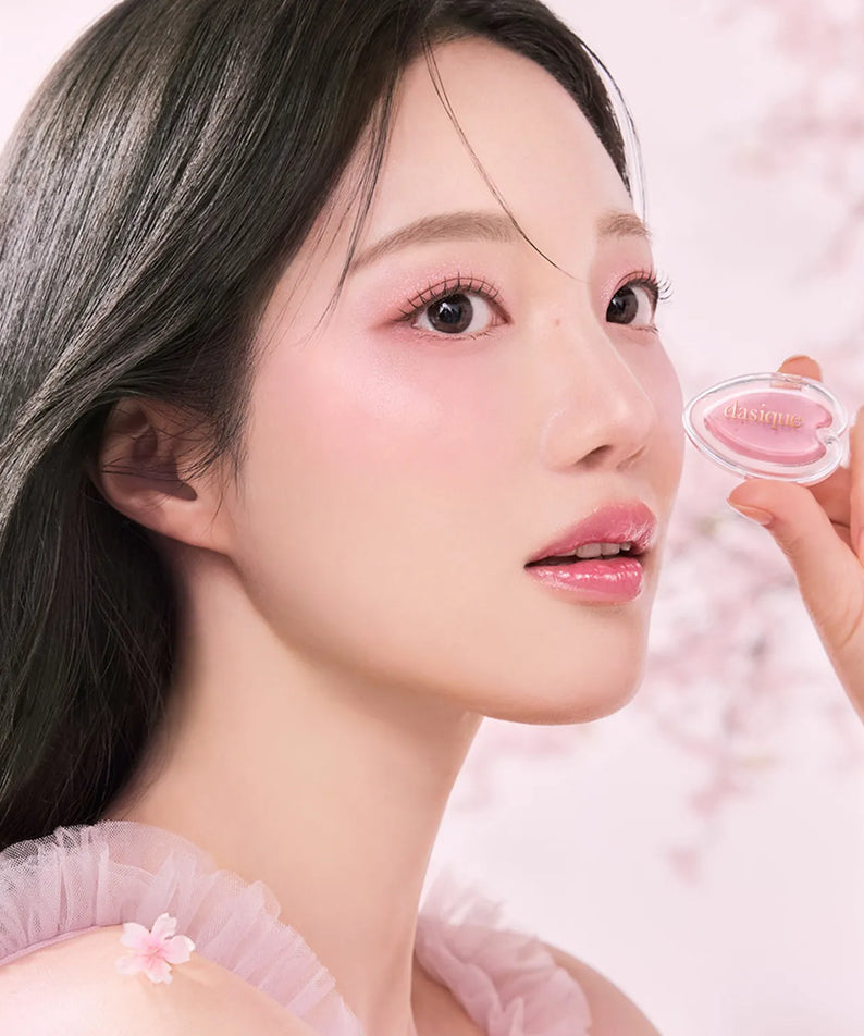 Woman holding DASIQUE Blooming Single Shadow with pink floral background, highlighting soft makeup look.