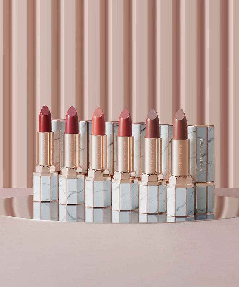 Collection of DEAR DAHLIA Lip Paradise Sheer Dew Lipstick in various shades, displayed elegantly on a reflective surface.