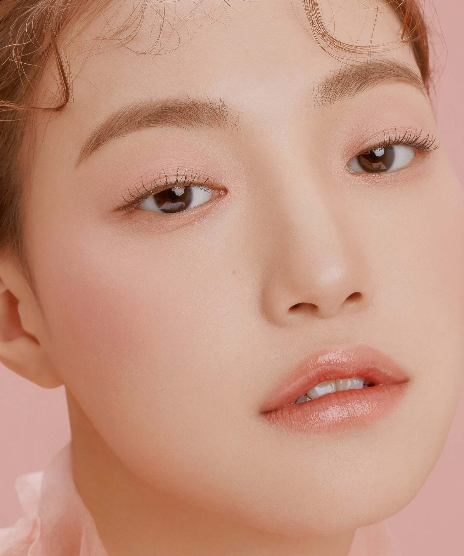 Close-up of a woman's face showcasing natural beauty, wearing DEAR DAHLIA Paradise Blooming Night makeup on a soft pink background.
