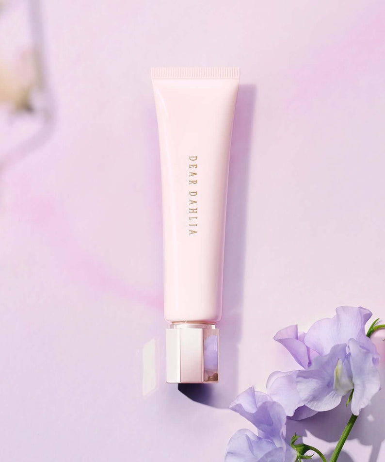 DEAR DAHLIA Prime Layer Blurring Primer tube on a pastel pink background with purple flowers for beauty and makeup enthusiasts.